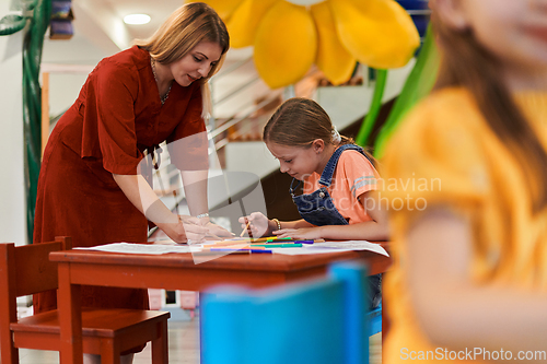 Image of Creative kids during an art class in a daycare center or elementary school classroom drawing with female teacher.