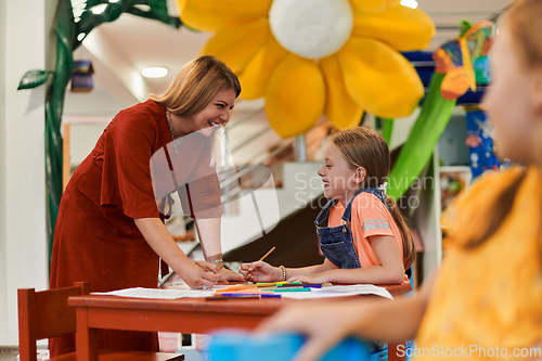 Image of Creative kids during an art class in a daycare center or elementary school classroom drawing with female teacher.