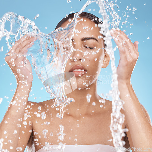 Image of Woman, hands or washing face in water splash on blue background studio for dermatology healthcare, hygiene wellness or self care grooming. Beauty model, facial cleaning or wet water drops in bathroom