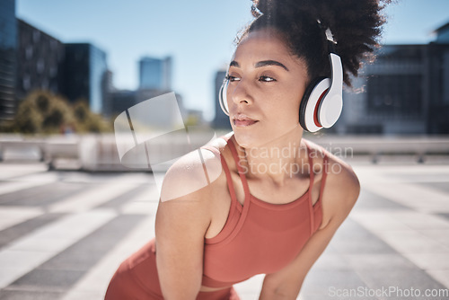 Image of Fitness, headphones and rest, woman runner stop to relax or breathe on city run or workout. Health, urban training and wellness, a tired black on break from running exercise while streaming music app