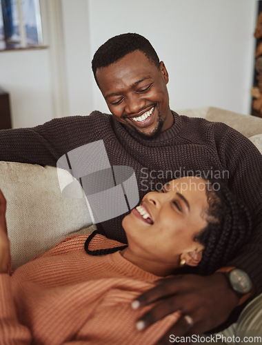 Image of Relax, laugh and together with a black couple bonding on a sofa in the living room of their home. Love, fun and humor with a man and woman joking, laughing or enjoying free time in the house