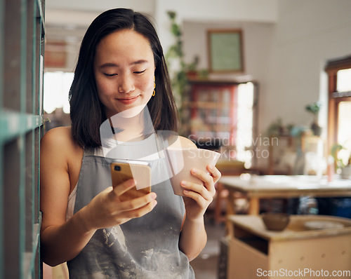 Image of Artist woman, phone and reading chat with coffee, smile and focus on email, app or social media for date. Asian art entrepreneur, social network and smartphone with happiness, tea and relax in studio