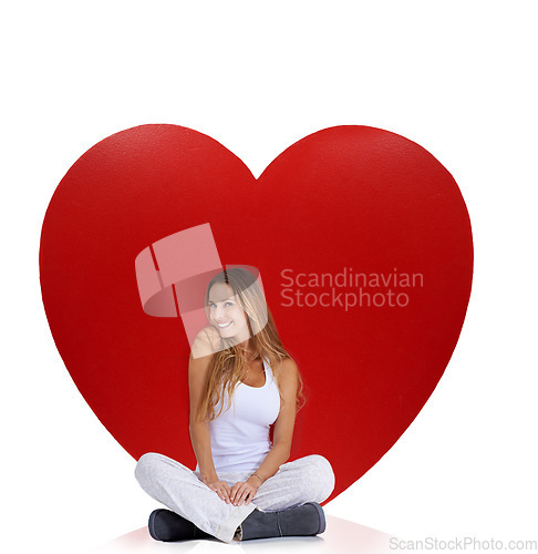 Image of Portrait, studio and woman sitting by heart isolated on a white background. Beauty, love and smile of happy female model near big symbol for romance, affection or romantic emoji, care or empathy.