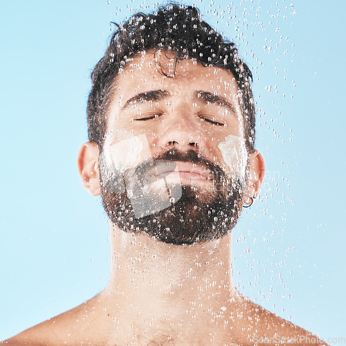 Image of Water, man with face and cream for cleaning in shower with hygiene, grooming and skincare against blue studio background. Clean, model with water drops and facial, natural treatment and cosmetic care