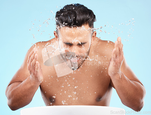 Image of Face, water splash and skincare of man cleaning in studio isolated on a blue background. Hygiene, water drops and male model washing, bathing or grooming for healthy skin, facial wellness or beauty.