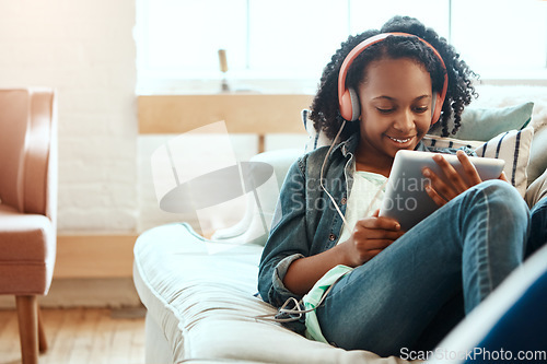 Image of Digital tablet, headphones and black woman on the sofa to relax while listening to music, radio or podcast. Rest, technology and African lady watch a video on mobile device in her living room at home