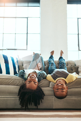 Image of Black children, siblings and relax on living room sofa lying upside down with smile for fun time together at home. Happy African American kids relaxing, playing and smiling on couch at the house