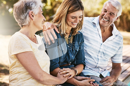 Image of Senior couple in nature with their adult daughter sitting, talking and bonding together in a garden. Happy, love and elderly people embracing child with care, happiness and affection in outdoor park.