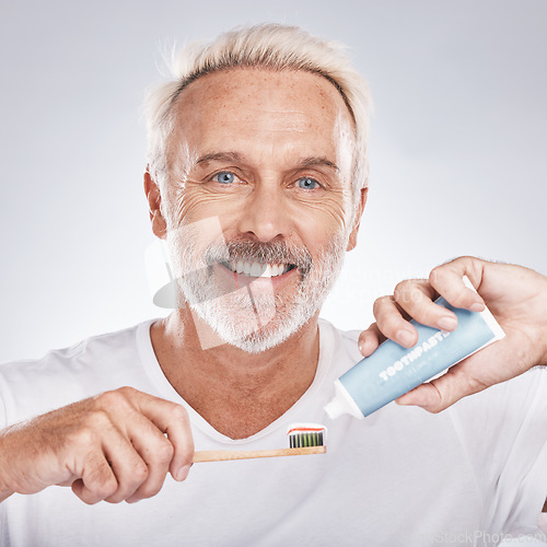 Image of Toothbrush, face and senior man with toothpaste in studio on a gray background. Portrait, cleaning and elderly male model holding product for brushing teeth, dental wellness and healthy gum hygiene.