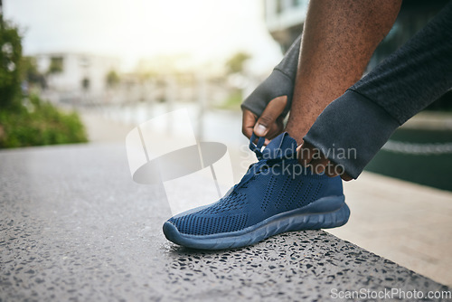 Image of Hands, fitness and black man tie shoes in city and getting ready for running, workout or exercise. Sports, wellness and male runner tying sneaker lace and preparing for training on street outdoors.