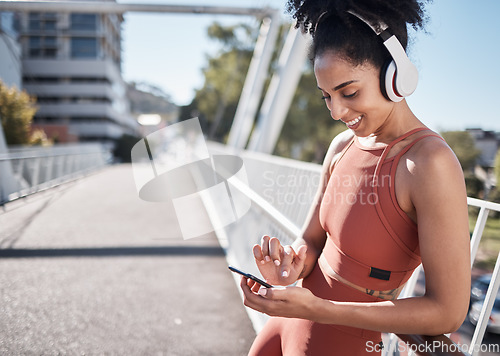 Image of Fitness, headphones and black woman with phone in city for social media or texting. Sports, exercise and happy female on break streaming music, radio or podcast on 5g mobile smartphone after training