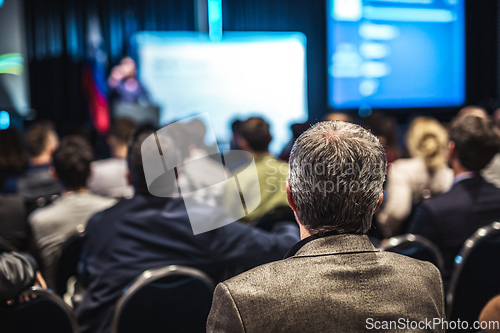 Image of Speaker giving a talk in conference hall at business event. Rear view of unrecognizable people in audience at the conference hall. Business and entrepreneurship concept.