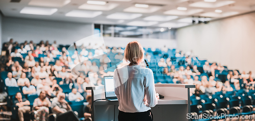 Image of Female speaker giving a talk on corporate business conference. Unrecognizable people in audience at conference hall. Business and Entrepreneurship event.