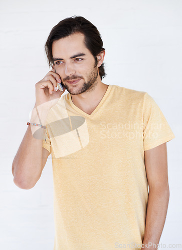 Image of Man, phone and phone call in studio, happy and relax while standing against white background space. Young, handsome and casual guy enjoying call, conversation and speaking while chilling and isolated