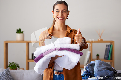 Image of Thumbs up, laundry and portrait of a woman maid folding clothes in the living room in a modern house. Happy, smile and female cleaner or housewife with a thumbsup cleaning or doing chores in a home.