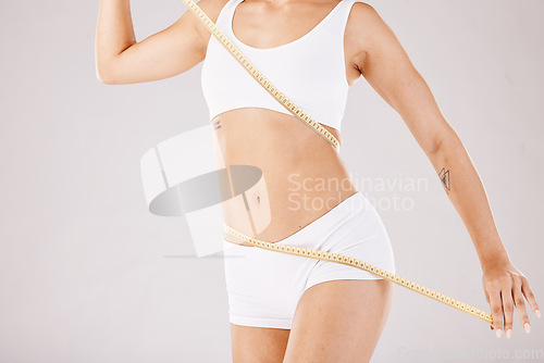 Image of Fitness, weightloss and slim woman in a studio with a measuring tape on her body for motivation. Diet, health and girl model with a healthy, wellness and exercise routine isolated by gray background.