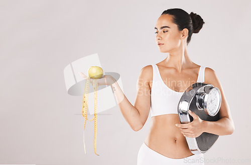 Image of Fitness, health and woman with scale and apple for weightloss, diet and nutrition on white studio background. Exercise, wellness and girl with fruit, balance and measuring tape for healthy lifestyle