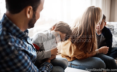 Image of Family, children and a father tickling his son in the living room of their home together with mom and brother in the background. Playful, relax or love with a man, woman and kids bonding in a house