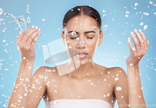 Image of Woman skincare, washing face or water splash on blue background studio for dermatology wellness, healthcare hygiene maintenance or grooming. Beauty model, hands or wet water drops for facial cleaning