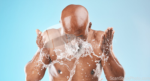 Image of Water splash, black man and facial skincare on blue background for shower, wellness and clean body care with personal hygiene. Male beauty, studio model and washing face with water drops in bathroom