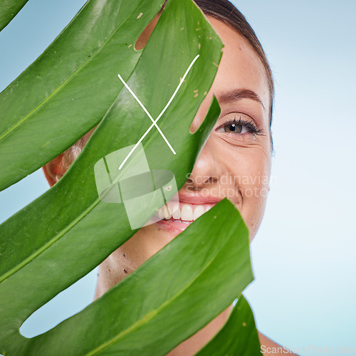 Image of Portrait, skincare and palm leaf with a model woman posing in studio on blue background for beauty. Face, skin or nature with an attractive young female standing behind a plant for natural treatment