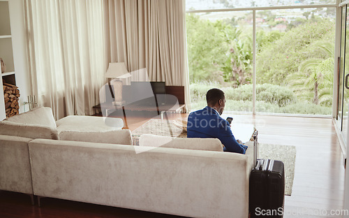 Image of Phone, travel and hospitality with a business black man sitting on a sofa in the living room of a hotel with his luggage. Back, bag and communication with a male employee typing a text message