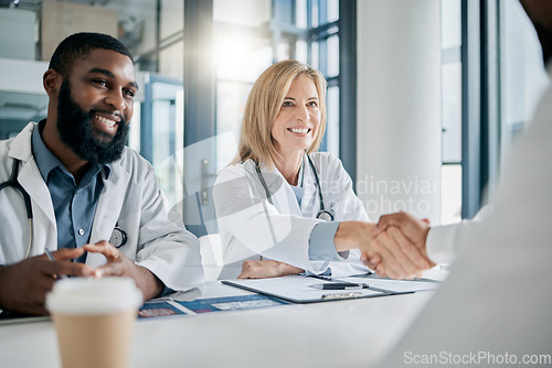 Image of Handshake, partnership or happy doctors in a meeting after successful medical surgery or reaching healthcare goals. Teamwork, woman or black man smiles shaking hands with a worker in hospital office