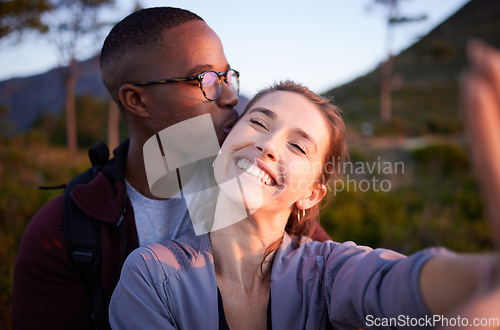 Image of Interracial couple, kiss and smile for selfie, travel or love for adventure, journey or hiking together in nature. Happy man kissing woman smiling in happiness for photo moments, trip or traveling