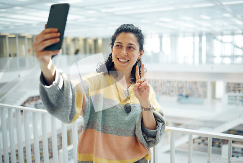 Image of Selfie, phone and peace with a woman in a library for research while posing for a social media photograph. Mobile, communication and hand gesture with a female student taking a picture in a bookstore