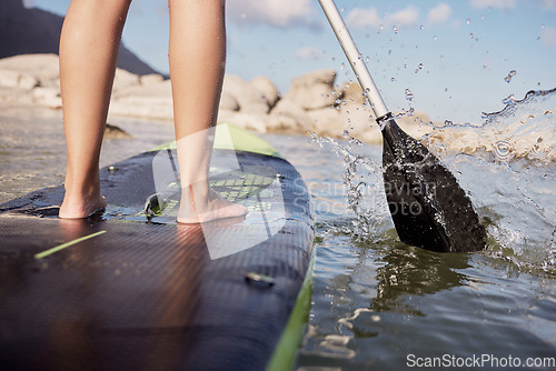 Image of Feet, paddle surf and water with a sports woman standing on a paddle board in the sea, ocean or a river outdoor. Back, balance and sport with a female athlete outside for fitness, exercise or hobby