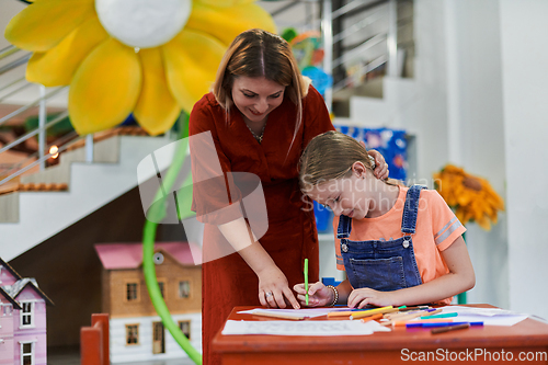 Image of Creative kids during an art class in a daycare center or elementary school classroom drawing with female teacher.