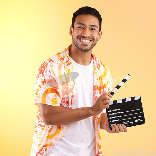 Image of Portrait, clapper board and man in studio isolated on a yellow background. Director, film production and happy male model in stylish or cool tie dye shirt holding clapperboard to cut scenes in movies