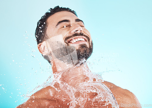 Image of Water, splash and skincare with face of man for shower, self care and natural cosmetics. Luxury, hydration and refreshing with model for dermatology, wellness and cleaning in blue background studio