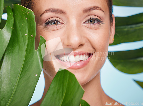 Image of Portrait, skincare and palm leaf with a model woman posing in studio on blue background for beauty. Face, skin or nature with an attractive young female standing behind a plant for natural treatment