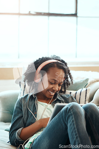 Image of Digital tablet, sofa and girl with headphones relaxing while listening to music, radio or podcast. Rest, technology and African child watching a video or movie on mobile device in living room at home