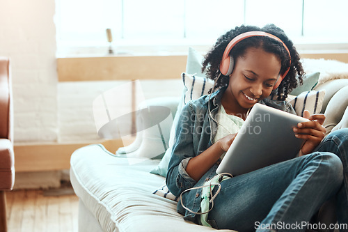 Image of Headphones, tablet and woman on the sofa to relax while listening to music, radio or podcast. Rest, technology and African lady watching a video or movie on mobile device in her living room at home.