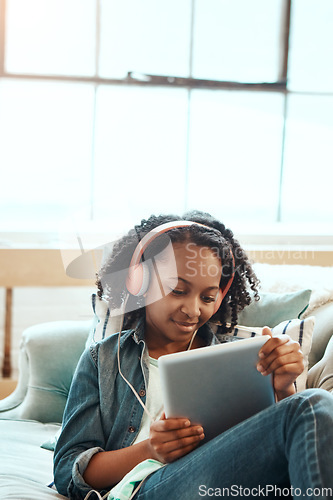 Image of Tablet, headphones and black girl on the sofa to relax while listening to music, radio or podcast. Rest, technology and African child watching a video or movie on mobile device in living room at home