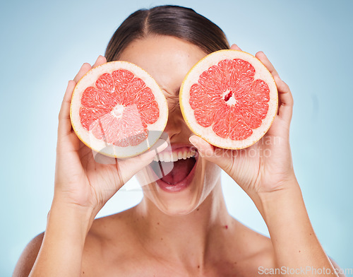 Image of Face, beauty skincare and woman with grapefruit in studio isolated on a blue background. Organic cosmetics, healthy diet and happy female model holding fruit for vitamin c, facial care and wellness.