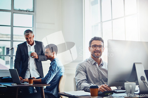 Image of Computer, portrait and businessman with his colleagues speaking in the background in the office. Technology, success and professional male employee working on a corporate project on a pc in workplace