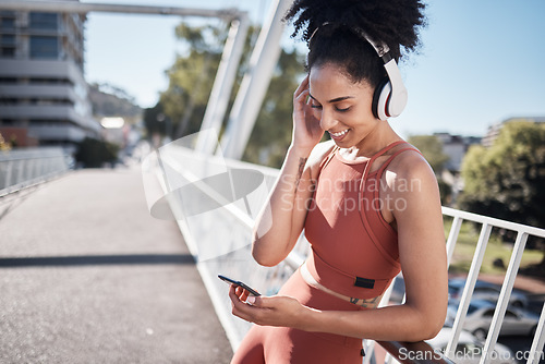 Image of Music headphones, fitness and black woman with phone for social media in city. Exercise, sports and female athlete streaming radio or podcast on 5g mobile smartphone after training outdoors on street