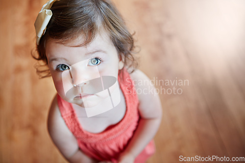 Image of Cute, adorable and little girl standing while looking up with sweet face on wooden floor at home. Portrait of small girl child, toddler or kid in pink dress, childhood or innocent youth at the house