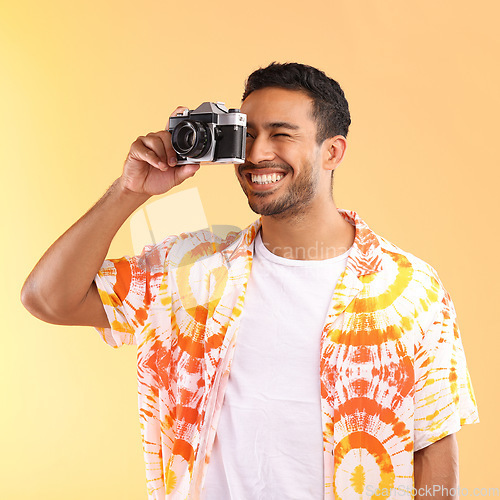 Image of Photographer, camera and man taking pictures in studio isolated on an orange background. Travel, vacation and male model holding camcorder technology for taking photo for happy memory on holiday.