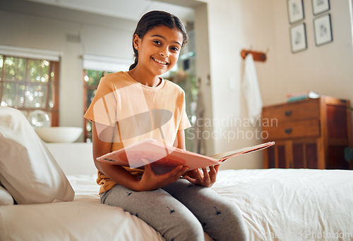 Image of Happy little girl, reading book and bed with smile for story time, education or learning in comfort at home. Portrait of cute female child smiling in happiness holding textbook to read in the bedroom