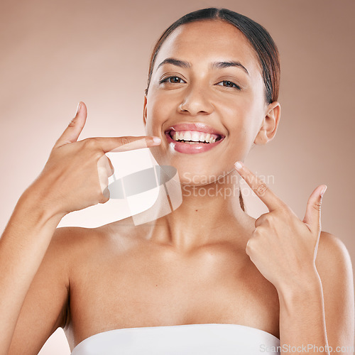 Image of Smile, face and woman pointing to teeth on studio background for wellness, aesthetic beauty or cosmetics. Portrait of model, dental health and showing clean mouth, fresh breath and happy oral results