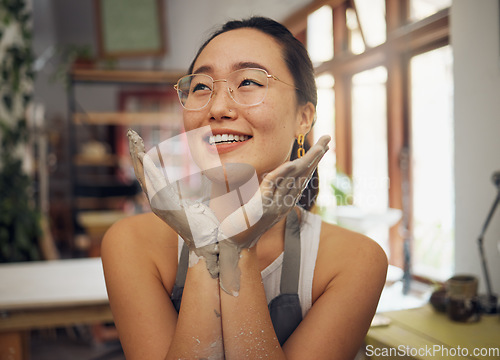 Image of Hands, face and dirty with an asian woman pottery professional sitting in her studio or workshop. Art, design and creative with a female designer or potter working in her clay or ceramics startup