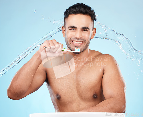 Image of Teeth, dental care and water splash, man with toothbrush and toothpaste on blue background with smile on face. Morning routine, healthcare and fresh studio portrait of model in India brushing teeth.
