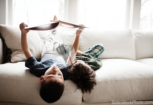 Image of Upside down, comfortable and children reading books on sofa for knowledge, information and education. Relax, content and boys with a story for happiness, studying and playing on the living room couch