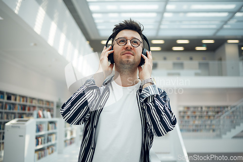 Image of Student, library and man with music headphones in university, college or school. Thinking, education scholarship and face of young male streaming educational podcast, radio or song, audio or album.