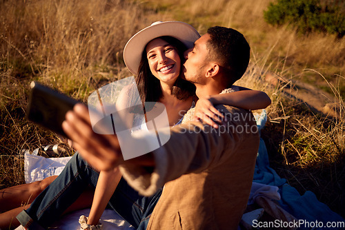 Image of Couple kiss in selfie with hug, outdoor and picnic in nature, love with smartphone, technology and happy together. Phone for photography, man and woman smile in picture with travel and summer date