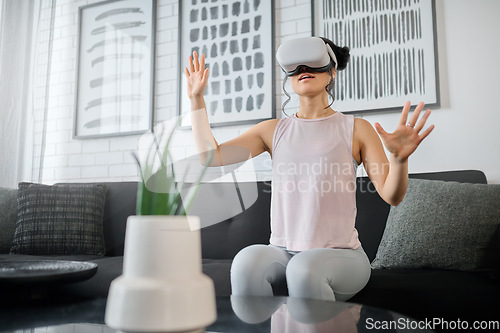 Image of VR, metaverse and technology with a woman in the living room of her home using a headset to access a 3d game. Futuristic, virtual reality and gaming with a female gamer using ai to access games